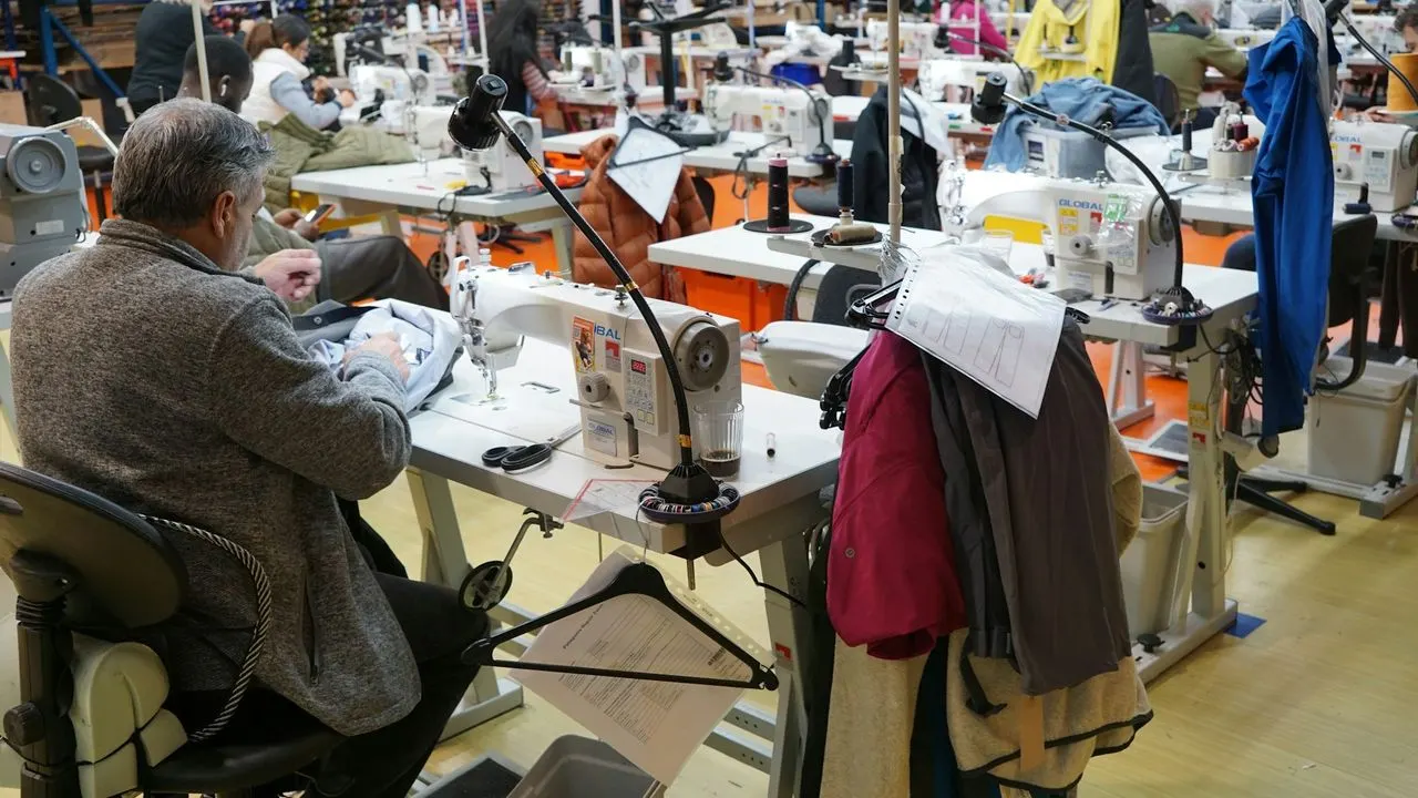 Sarto al lavoro con una macchina da cucire in un laboratorio affollato